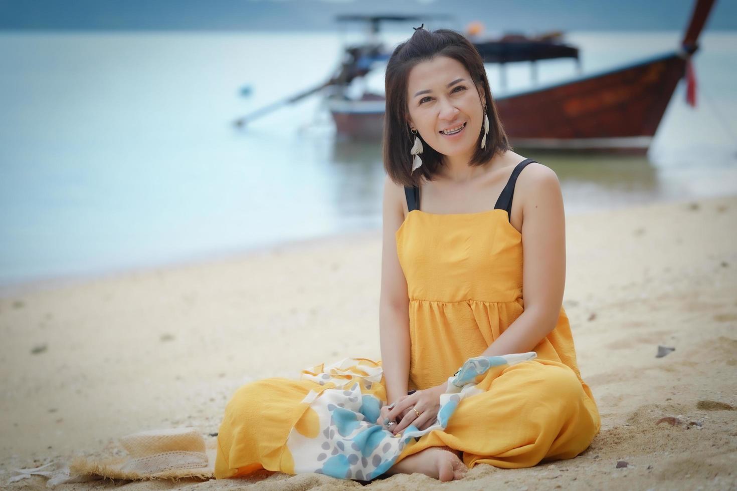 Portrait of a cute girl sitting on the beach with a blurred traditional long-tail boat in the background photo