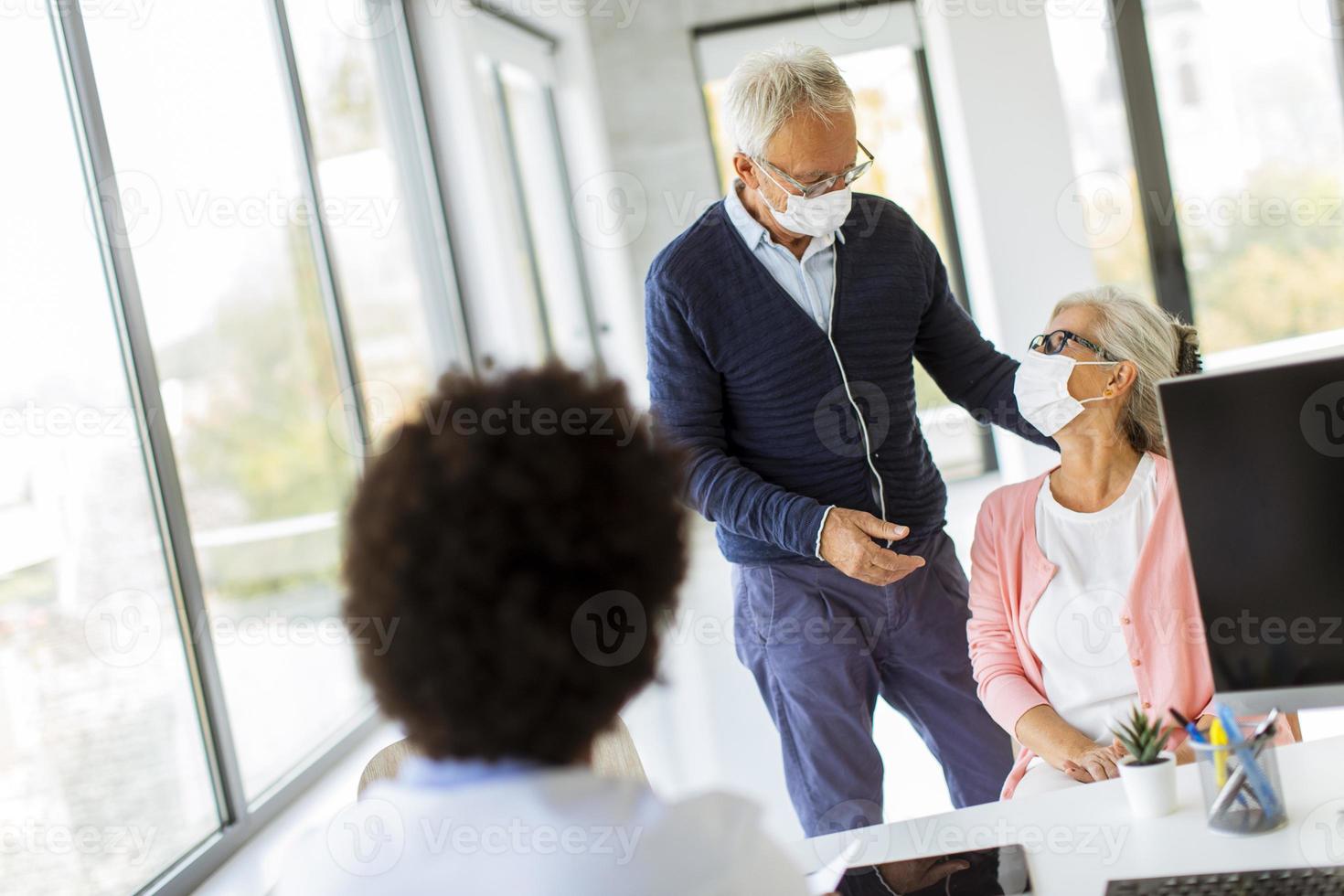 Mature couple wearing masks and talking to doctor photo