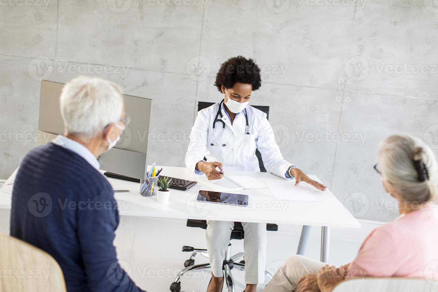 Doctor talking to mature couple with masks photo