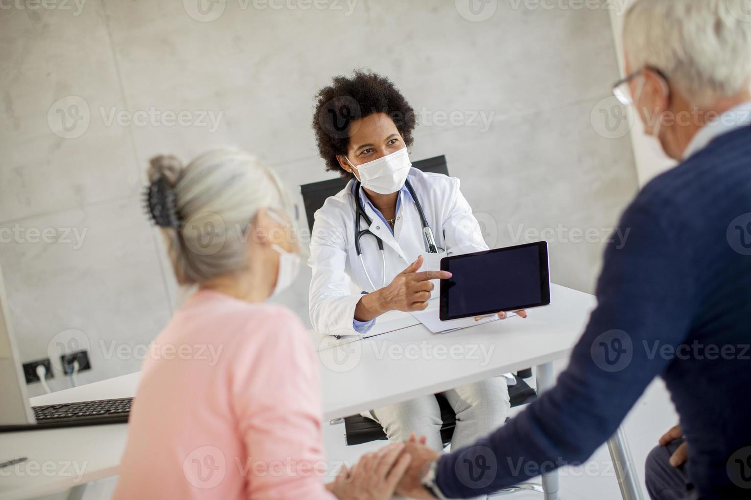 Doctor giving masked mature couple news photo