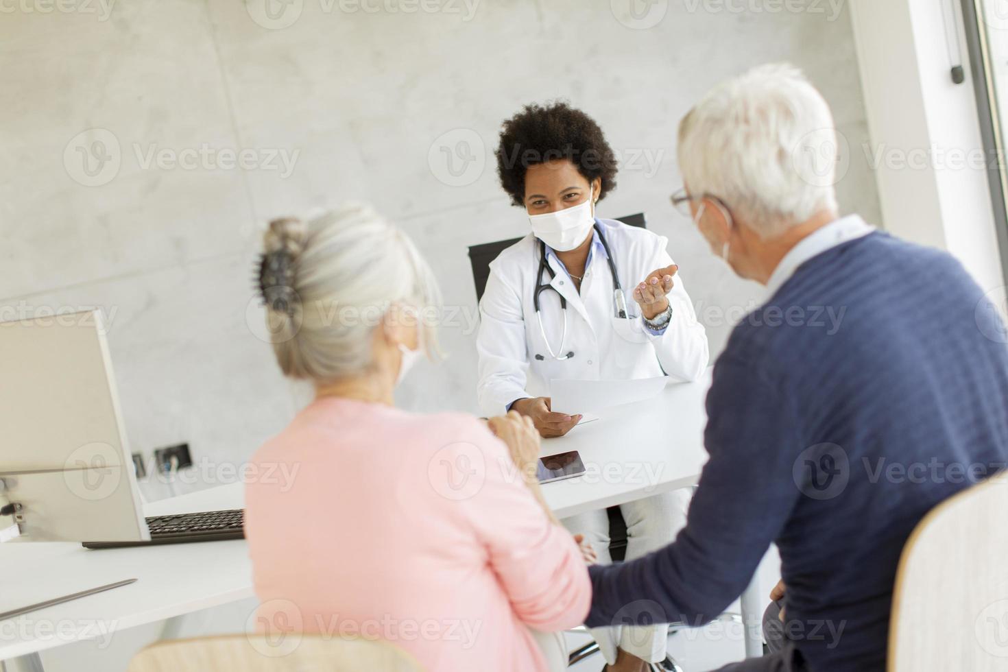 Masked mature couple speaking to doctor photo