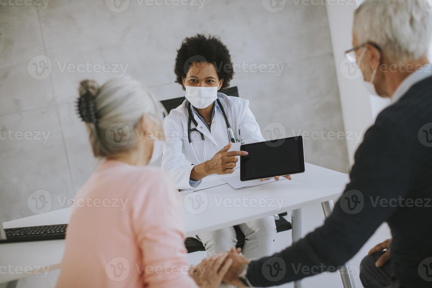 Mature couple in masks talking to doctor photo