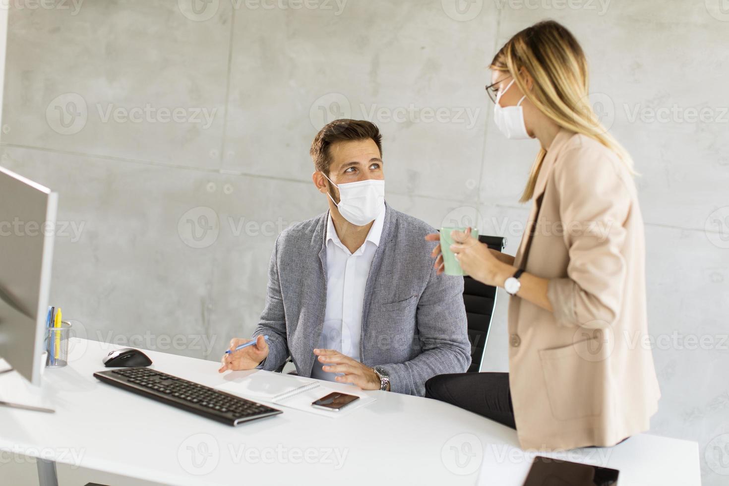 Two masked business people at desk photo