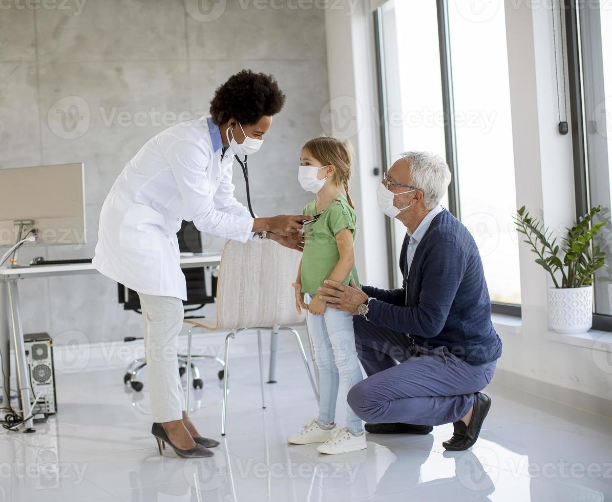 Doctor examining girl with grandparent photo