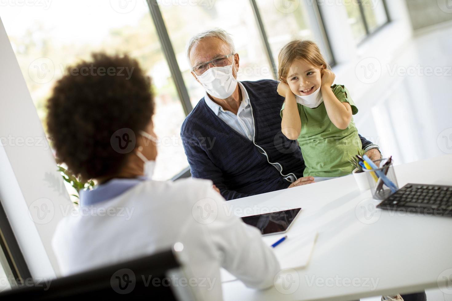 Doctor talking to masked grandparent and grandchild photo