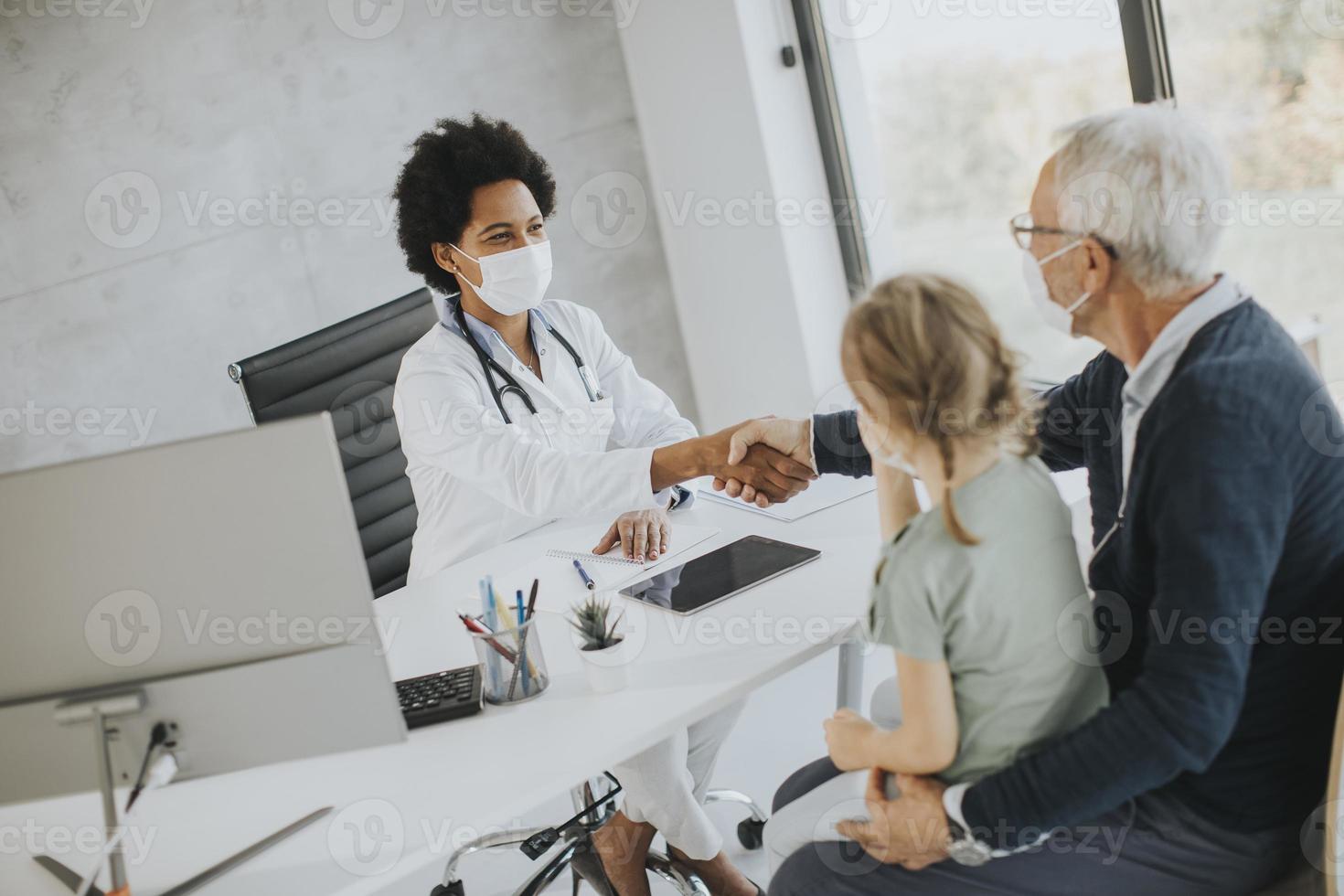 Doctor speaking to masked grandparent and grandchild photo
