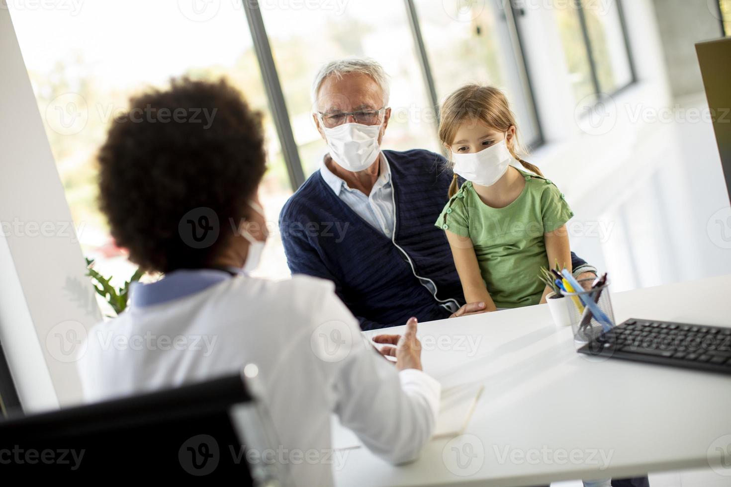 Masked grandfather and granddaughter talking to doctor photo