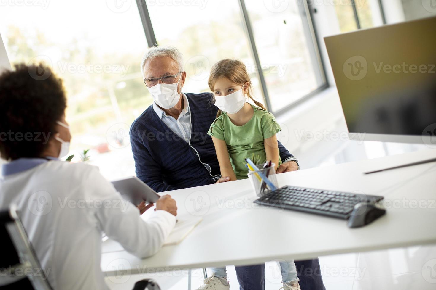 Abuelo y nieta enmascarados en el consultorio del médico moderno foto