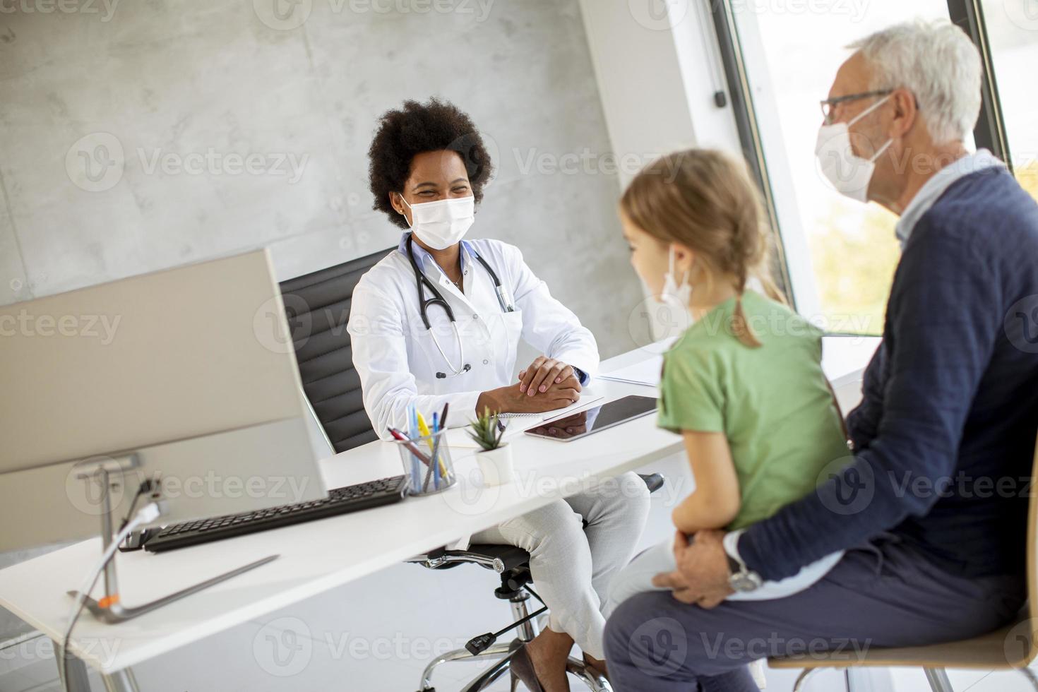 Doctor talking to masked grandfather and granddaughter photo