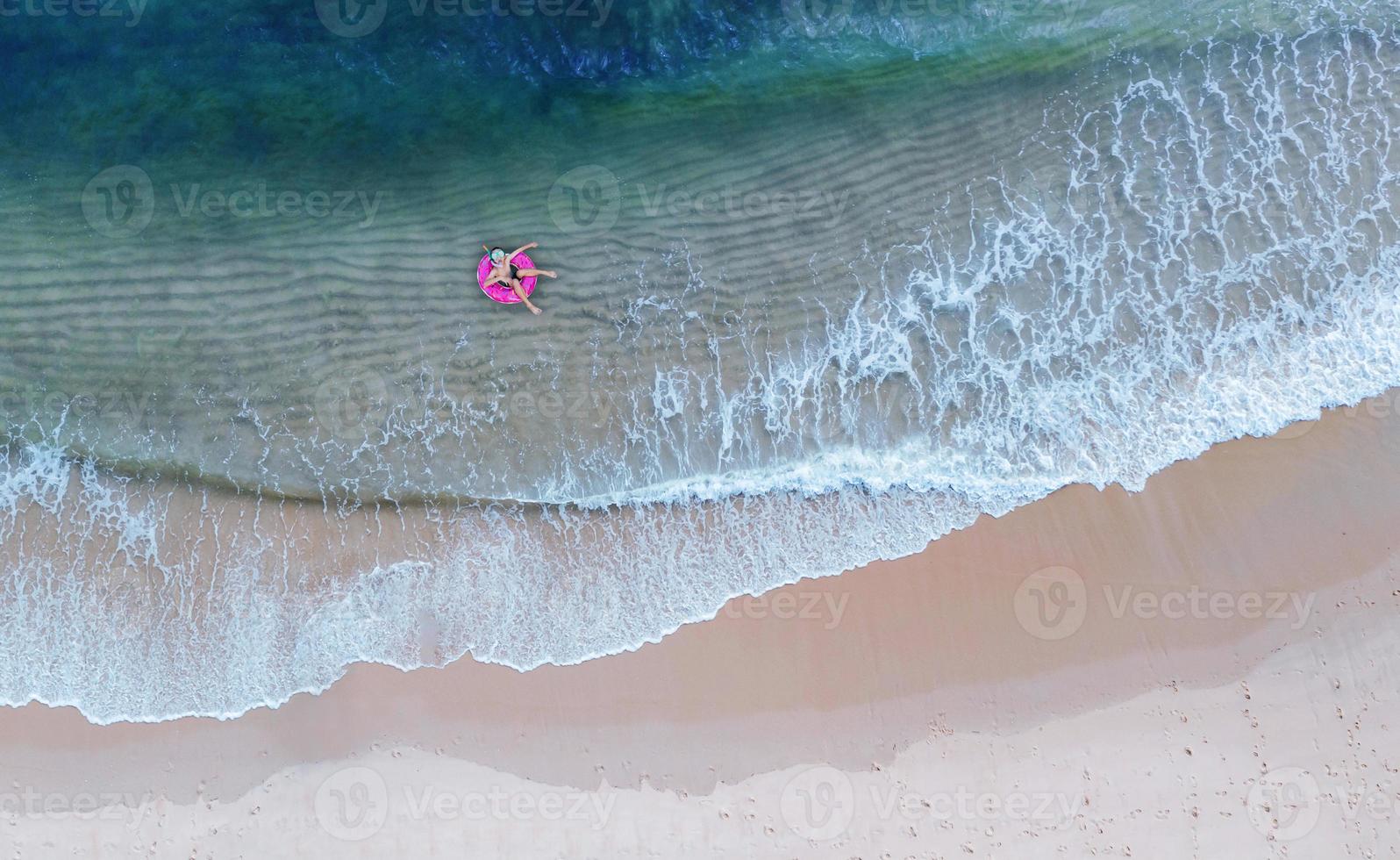 Vista aérea superior desde la vista aérea del niño con anillo de natación en el mar y sombra de agua azul esmeralda y espuma de olas al amanecer. foto