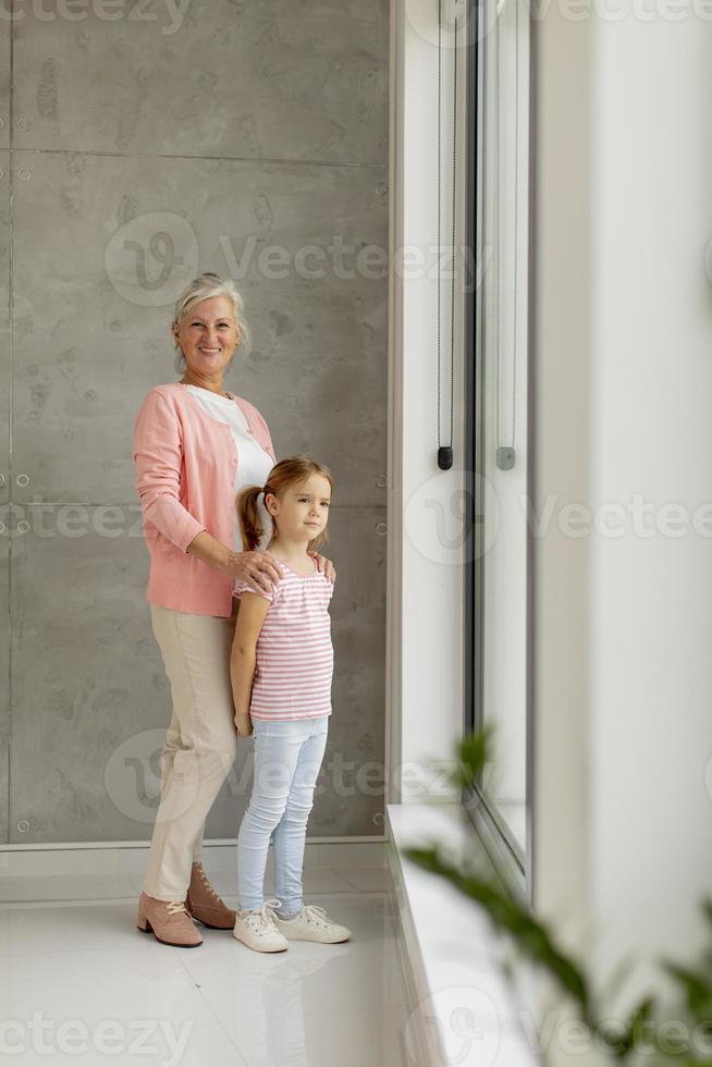 Vista vertical de una abuela y una nieta mirando por la ventana foto