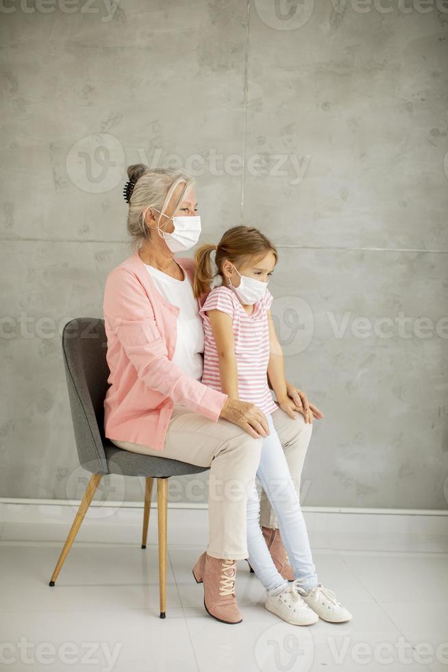 Vista vertical de una abuela sentada con una nieta con máscaras foto