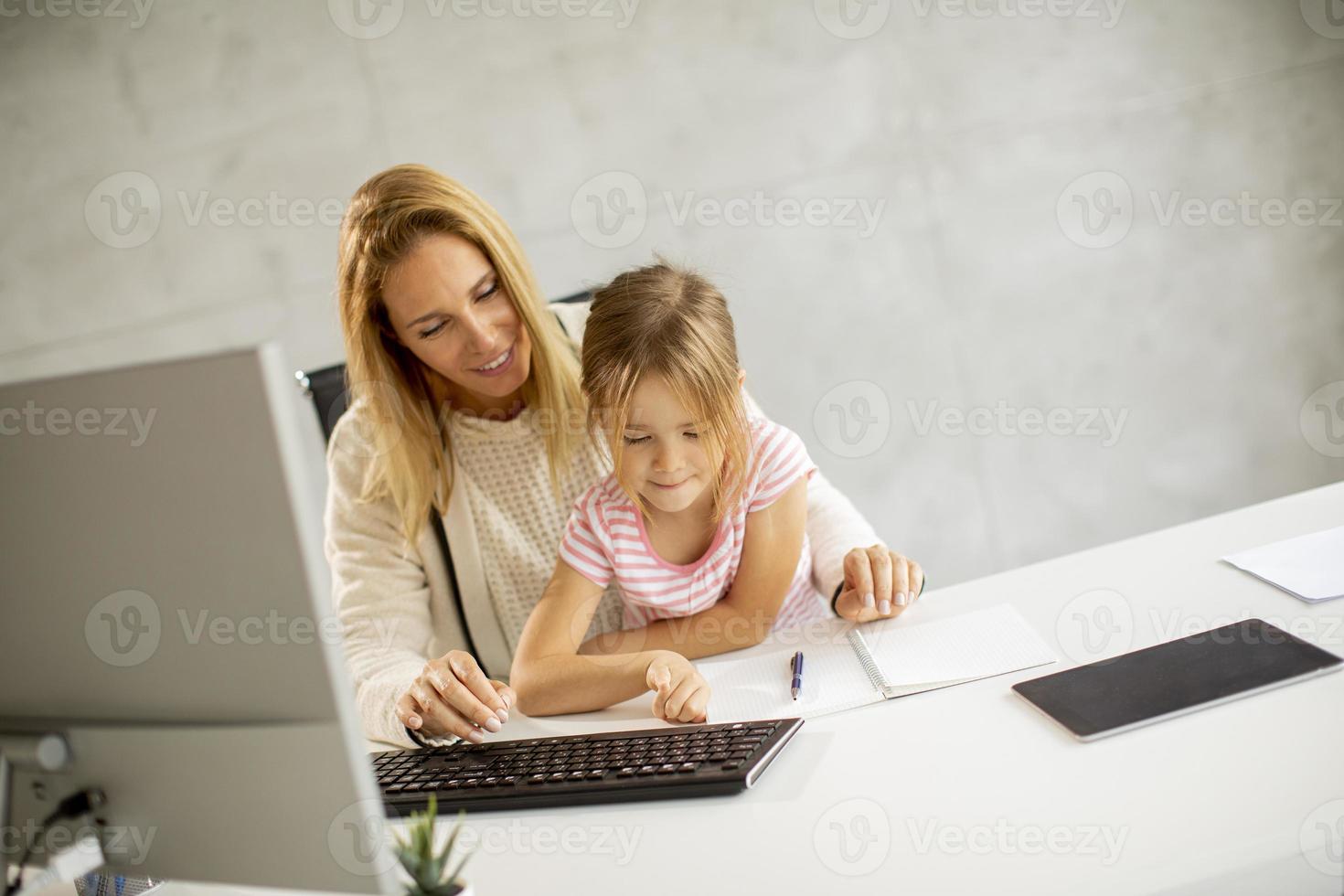 Mother trying to work with daughter on her lap photo