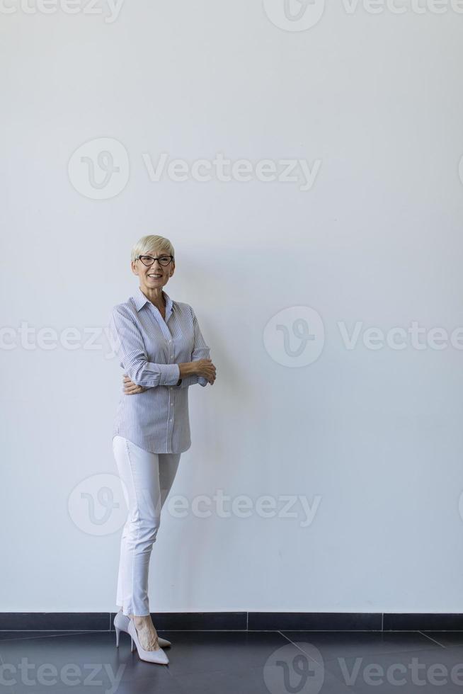 Mature businesswoman with arms crossed standing by wall photo