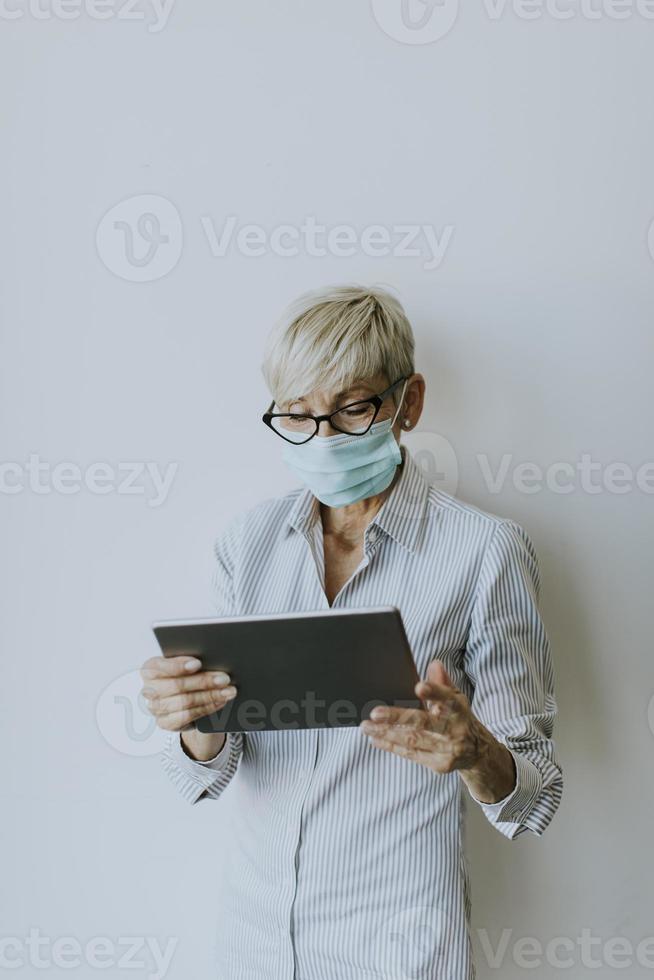 Vista vertical de una empresaria madura enmascarada usando una tableta foto