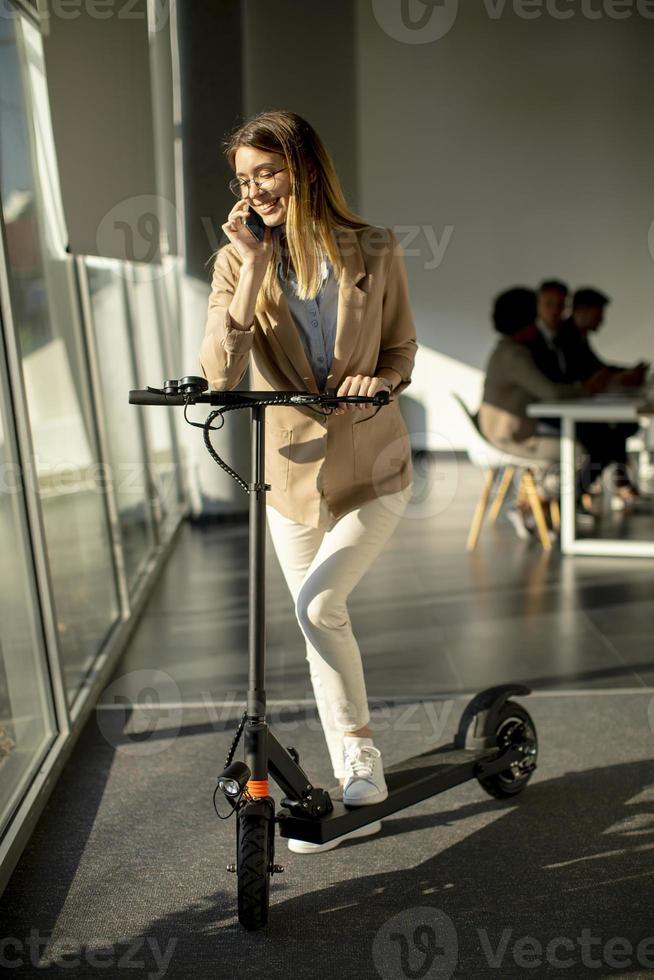 mujer, en, teléfono, con, scooter, en, oficina foto
