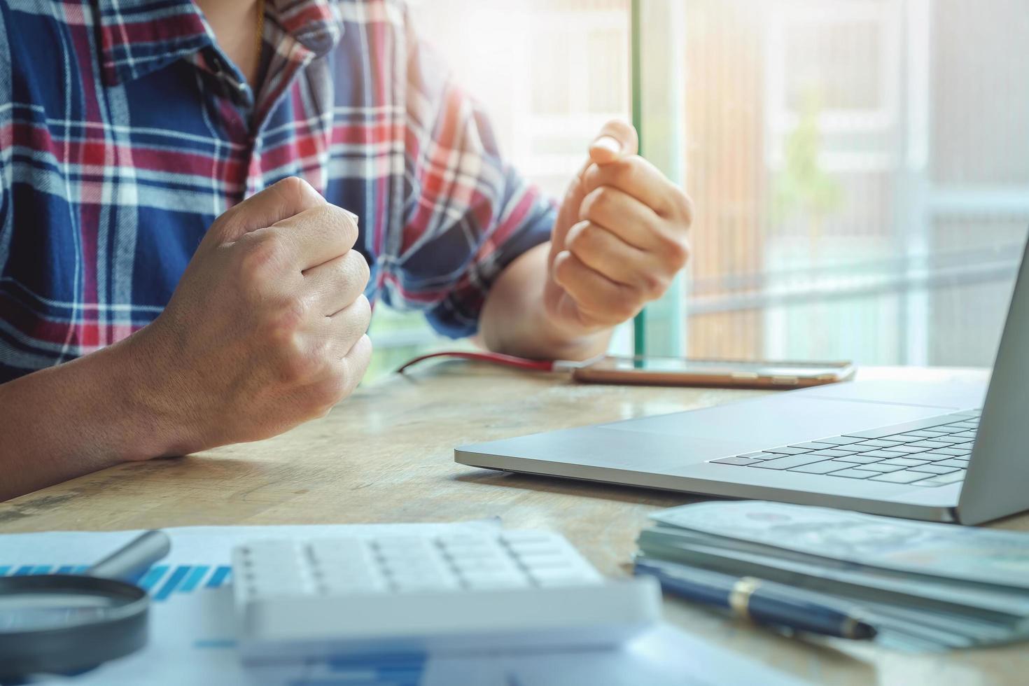 Hombres de negocios que muestran signos de alegría por el éxito de la inversión en acciones con el uso de una computadora portátil y una calculadora y el stock de datos en el análisis. foto