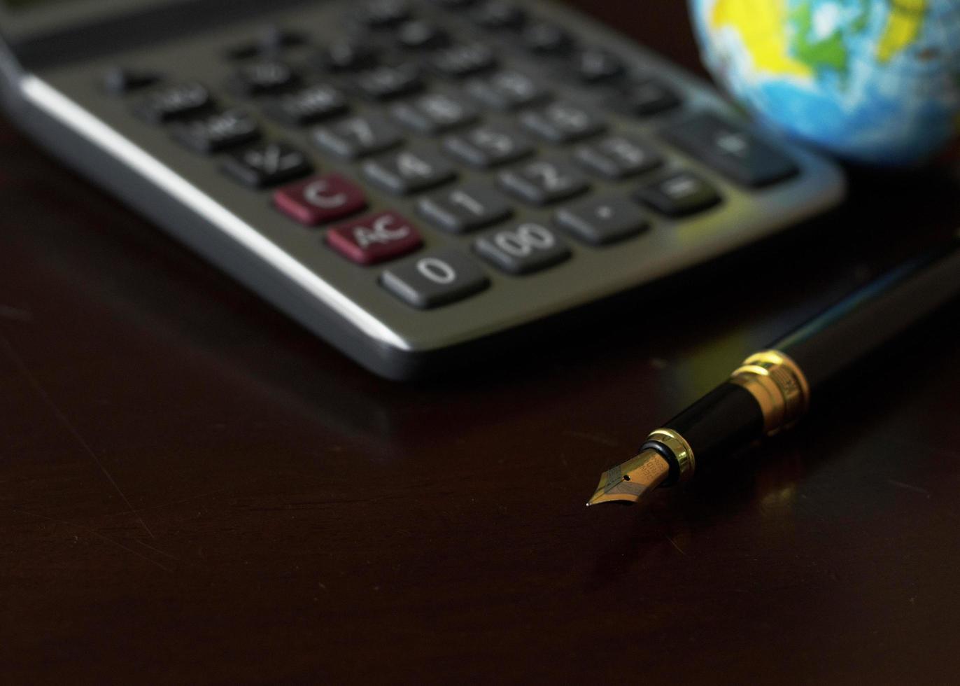 Pluma estilográfica, calculadora y fondo de globo terráqueo por concepto de negocio foto