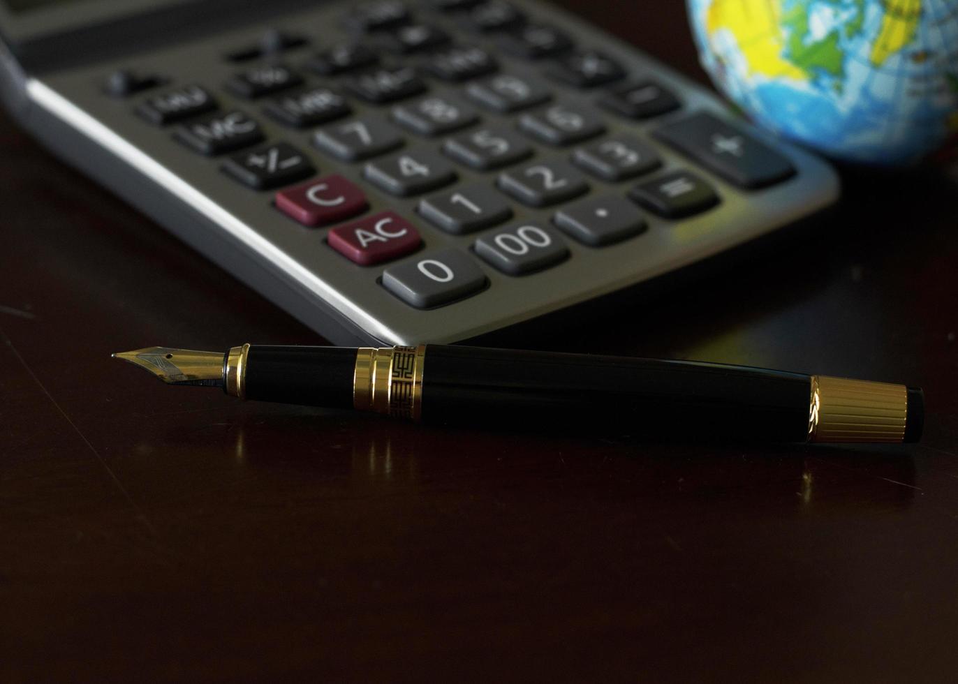 Fountain pen and calculator and earth globe on wooden table for business concept photo