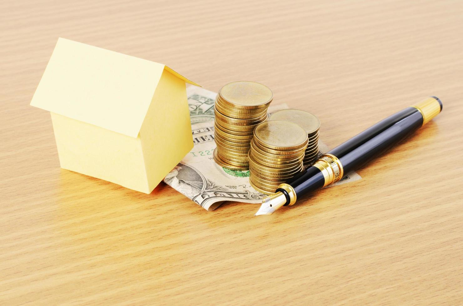 Home loans concept with house paper and fountain pen with dollar money coins stack on wooden desk background photo