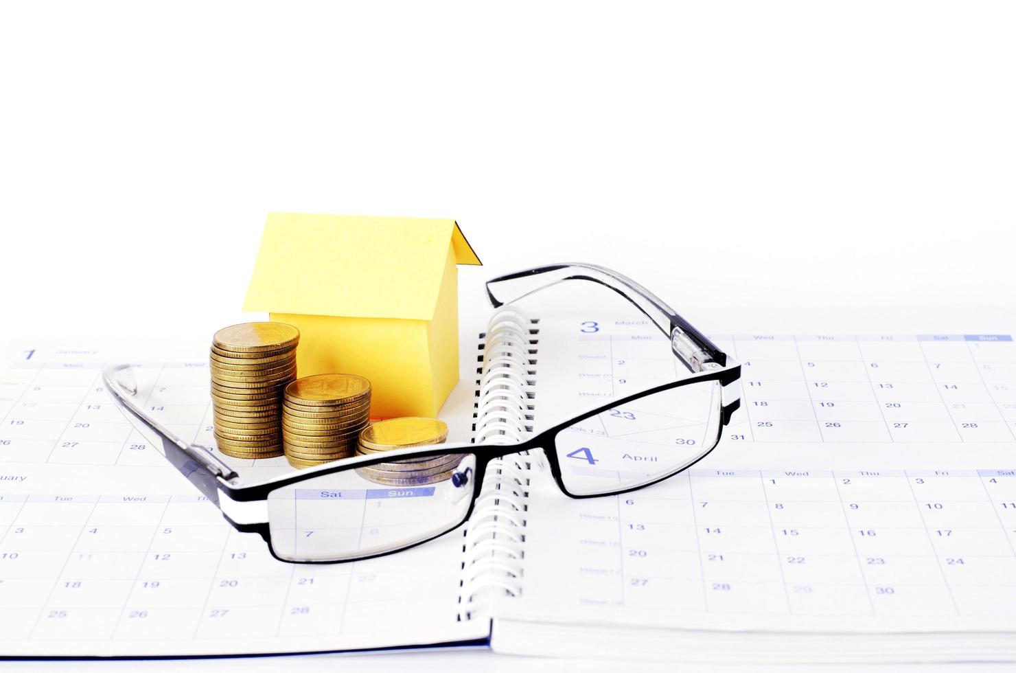 Loans concept with eyeglasses and money coins stack and paper house on calendar book pages photo