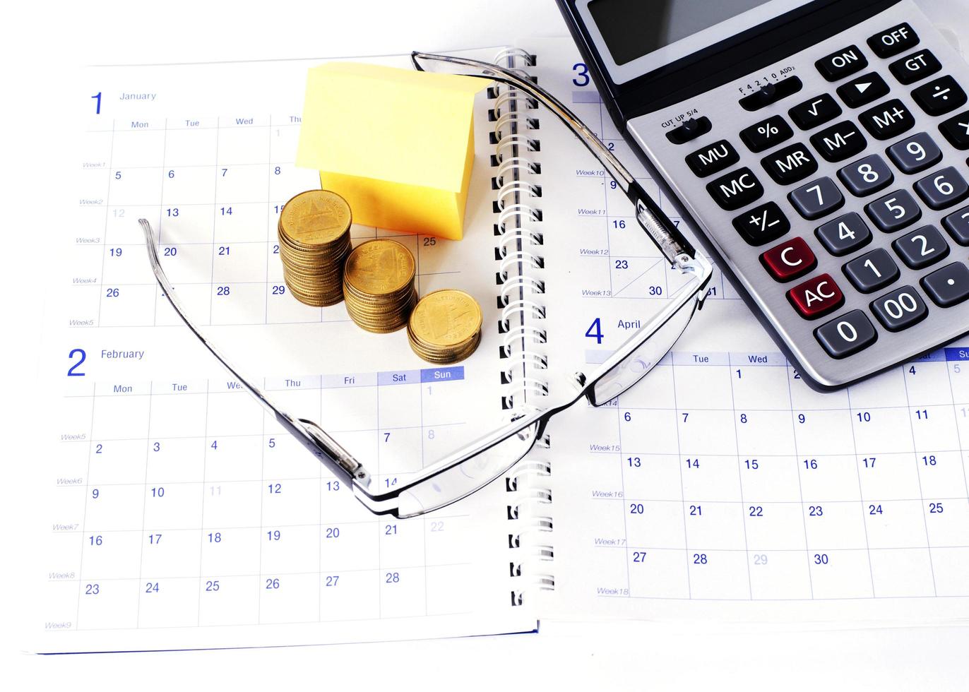 Business concept with eyeglasses and coins stack and paper house and calculator on calendar book pages photo