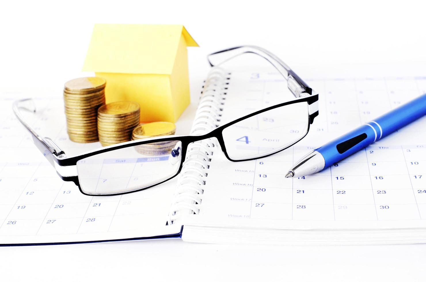 Loan concept with eyeglasses and pen and coins stack and paper house on book pages photo