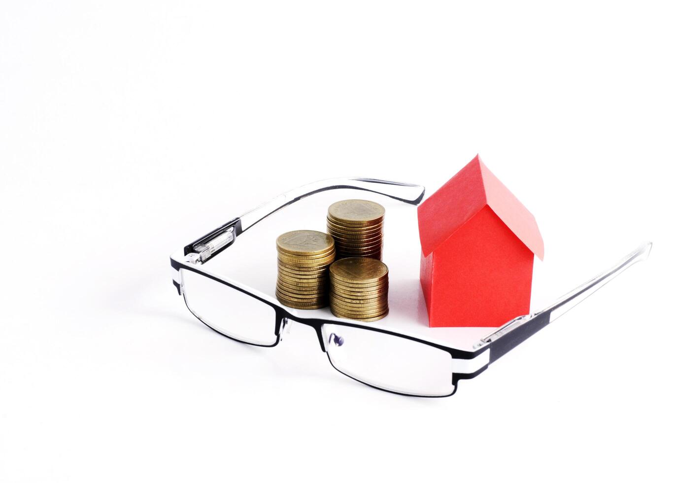 Red house paper and coins stack and eyeglasses on white background photo