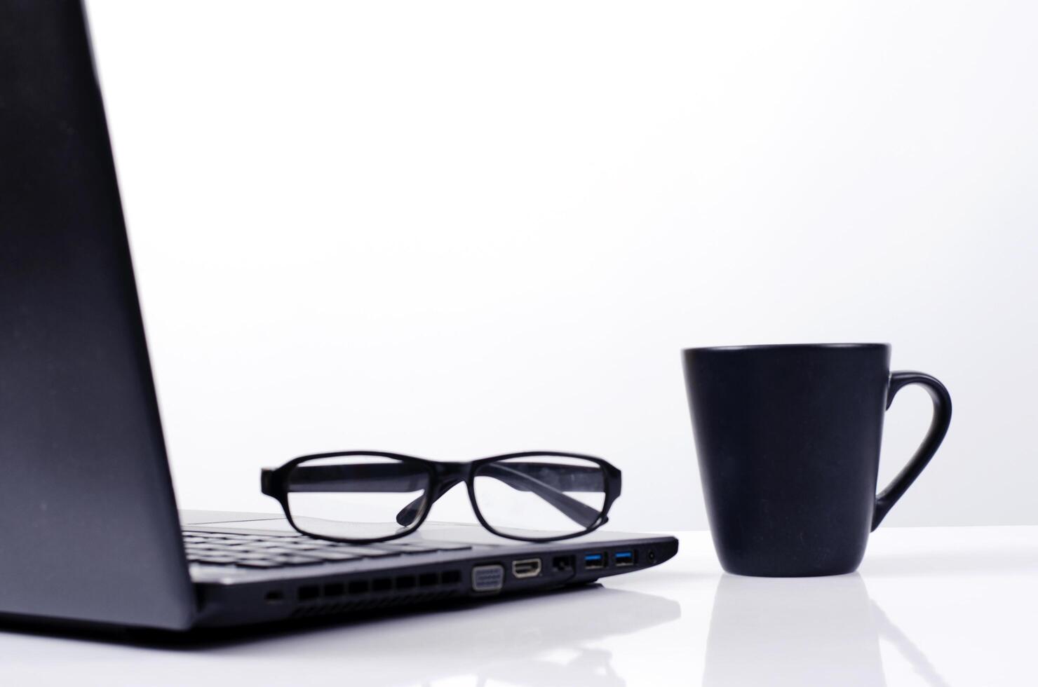 Black coffee cup and eyeglasses put on laptop on white background photo