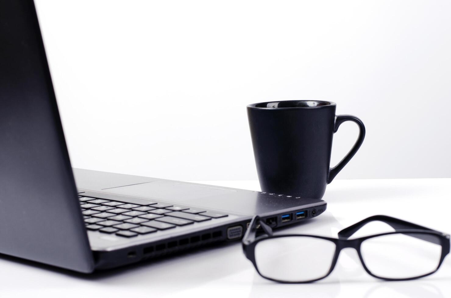 Cerca de tazas de café con equipo labtop y anteojos sobre fondos blancos foto