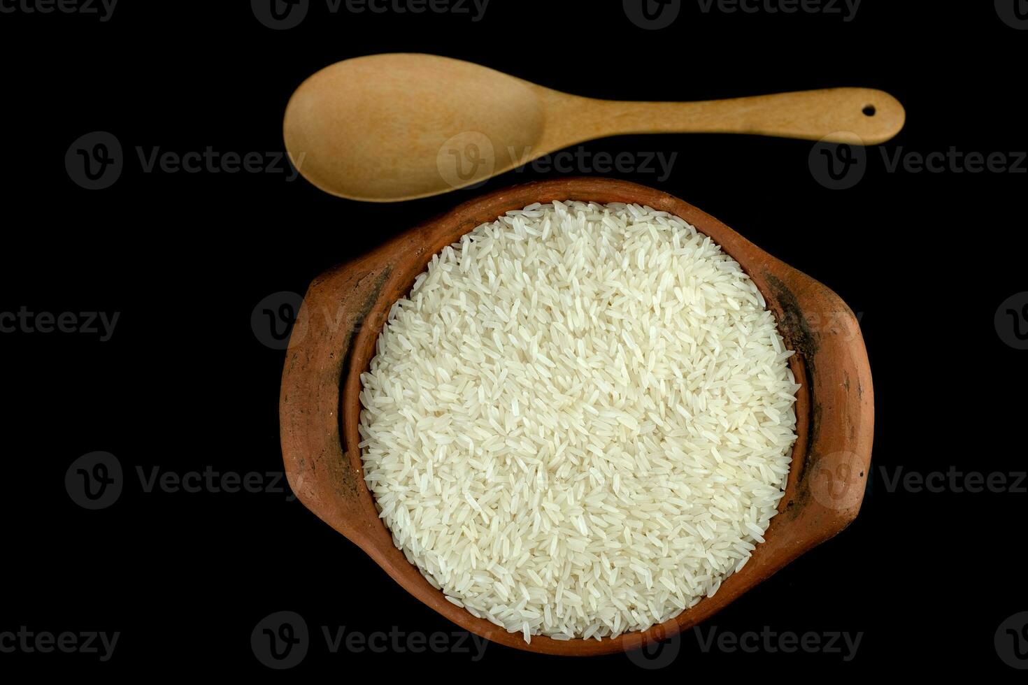 Jasmine rice in a clay pot and a wood ladle isolated on a black background photo