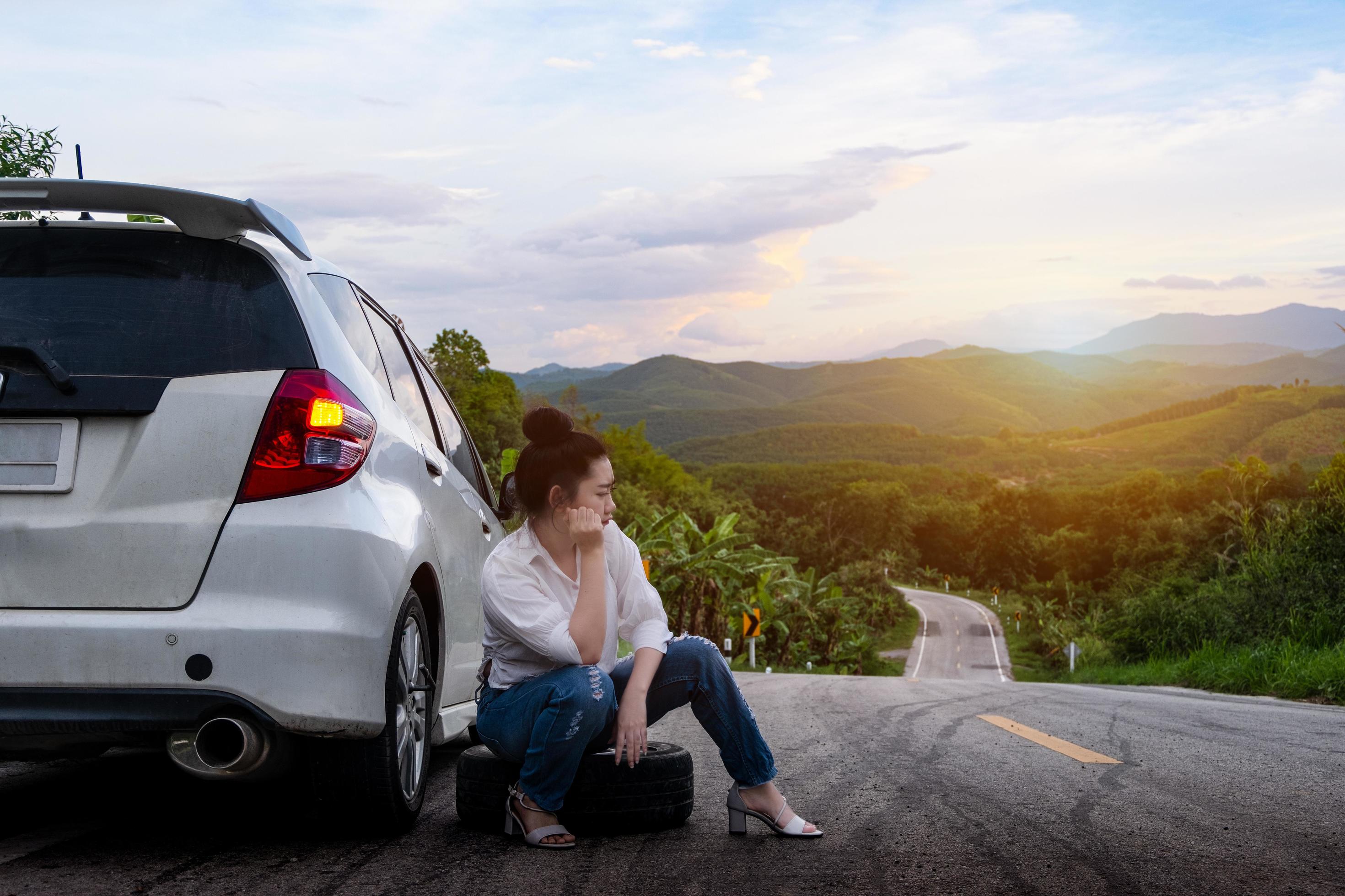 Young beautiful lady sitting near a car for calling for help on the public  road in a forest area with a mountain and sky background 2411555 Stock  Photo at Vecteezy