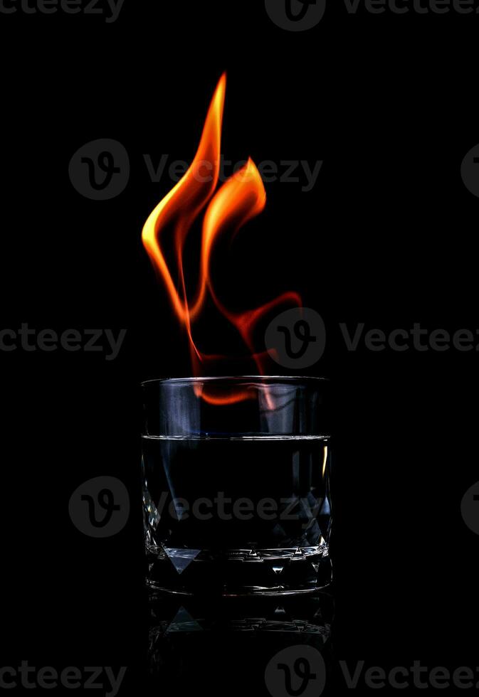 Vaso con vodka y llamas de fuego sobre un fondo negro foto