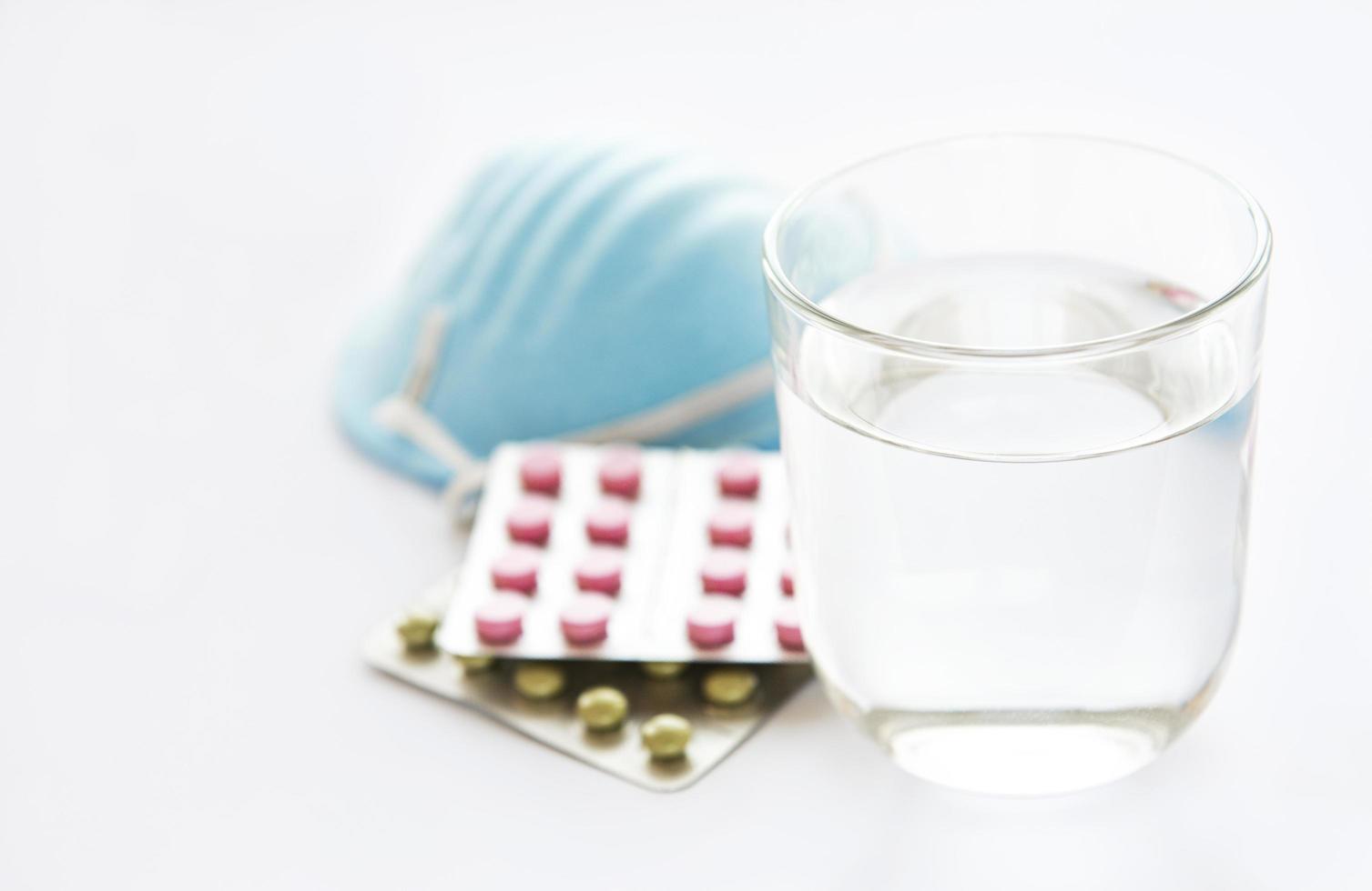 vaso de agua azul mascarilla médica y pastillas medicinales foto