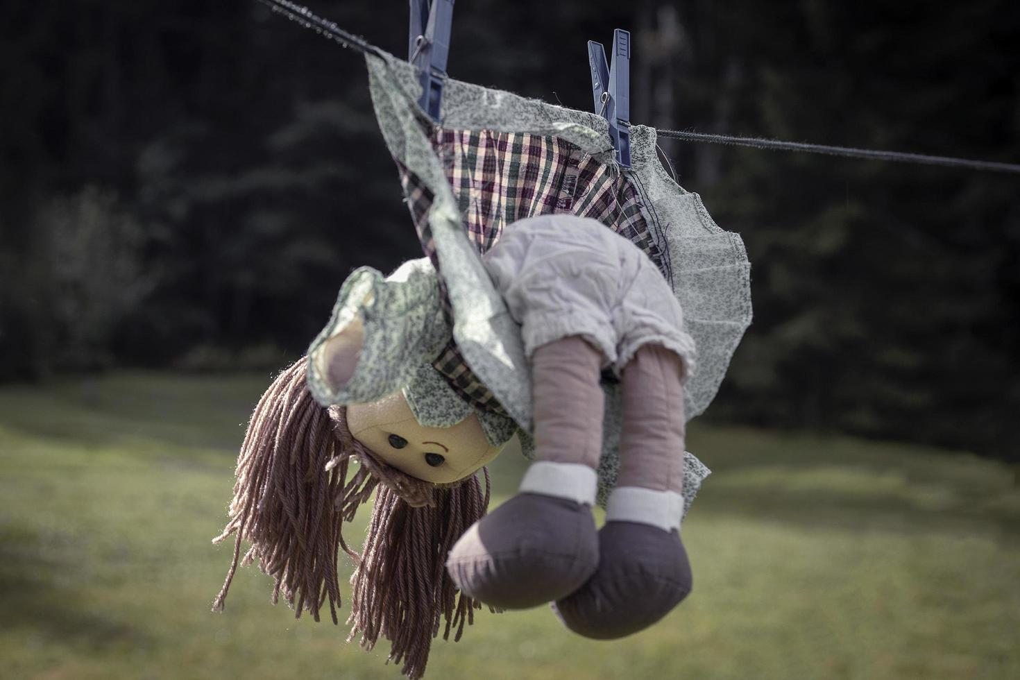 Concepto de violencia contra los niños, muñeca pelirroja abandonada en vestido colgando de una cuerda foto