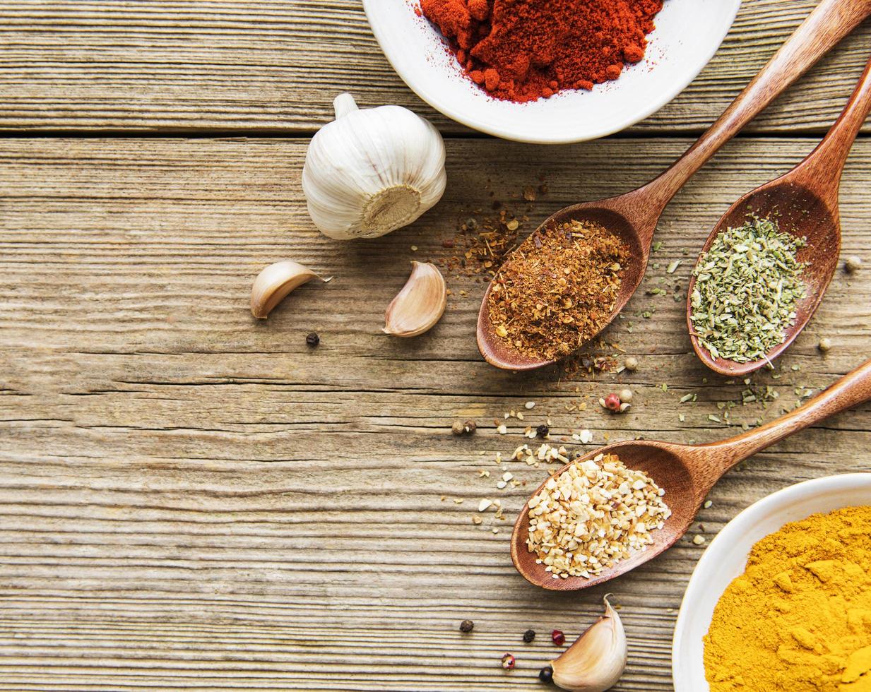 A selection of various colorful spices on a wooden table in bowls and spoons photo