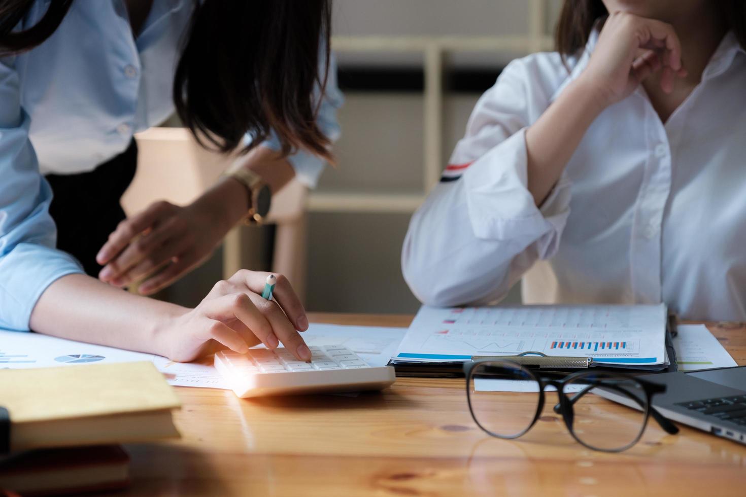 Close up of businesswoman using calculator for math and finance while discussing with customer on wooden desk. photo