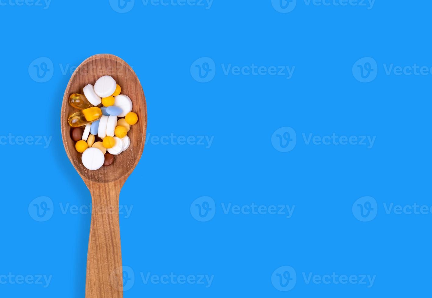 Pastillas de medicina en una cuchara de madera sobre fondo azul con espacio de copia foto