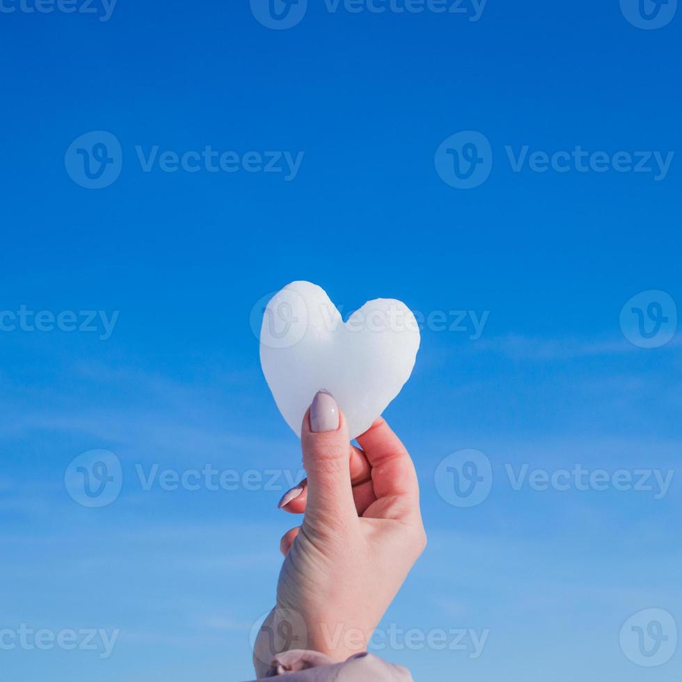 Manos femeninas con corazón blanco de nieve en día de invierno foto