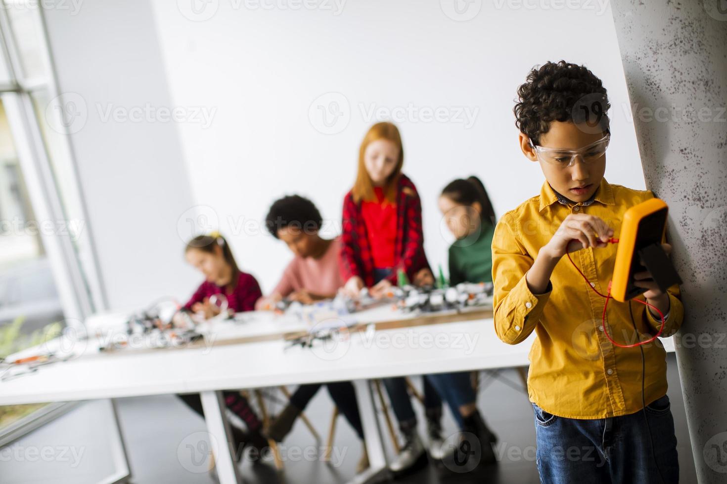 Cute little boy parado frente a los niños que programan juguetes eléctricos y robots en el aula de robótica foto