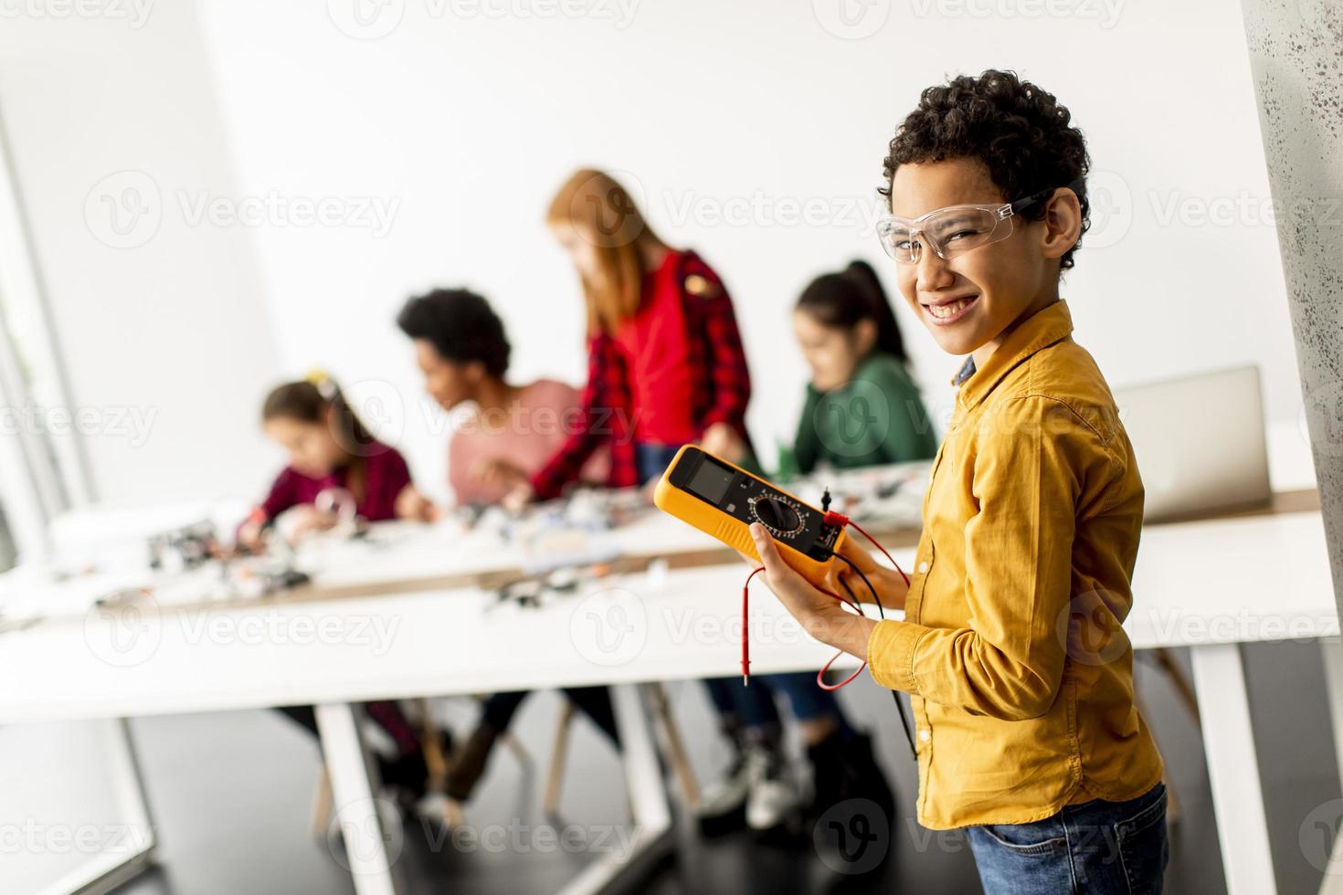 Cute little boy parado frente a los niños que programan juguetes eléctricos y robots en el aula de robótica foto