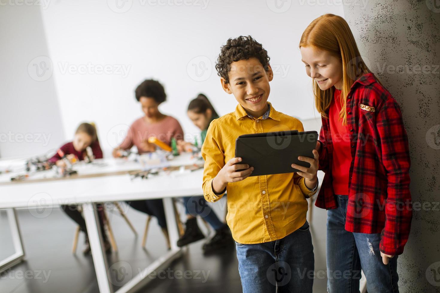 Best friends standing in front of kids programming electric toys and robots at robotics classroom photo