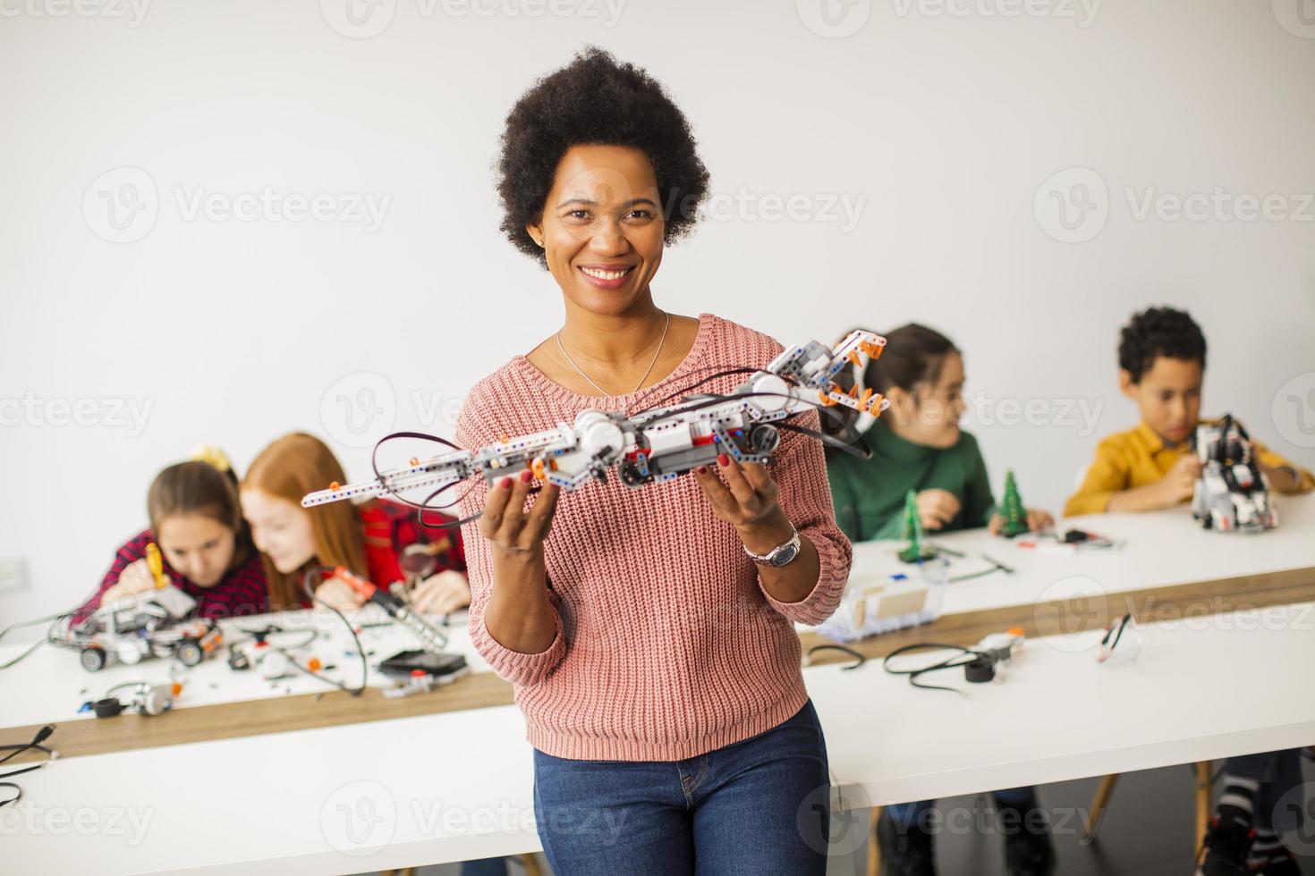 Niños felices con su profesora de ciencias afroamericana que programan juguetes eléctricos y robots en el aula de robótica foto