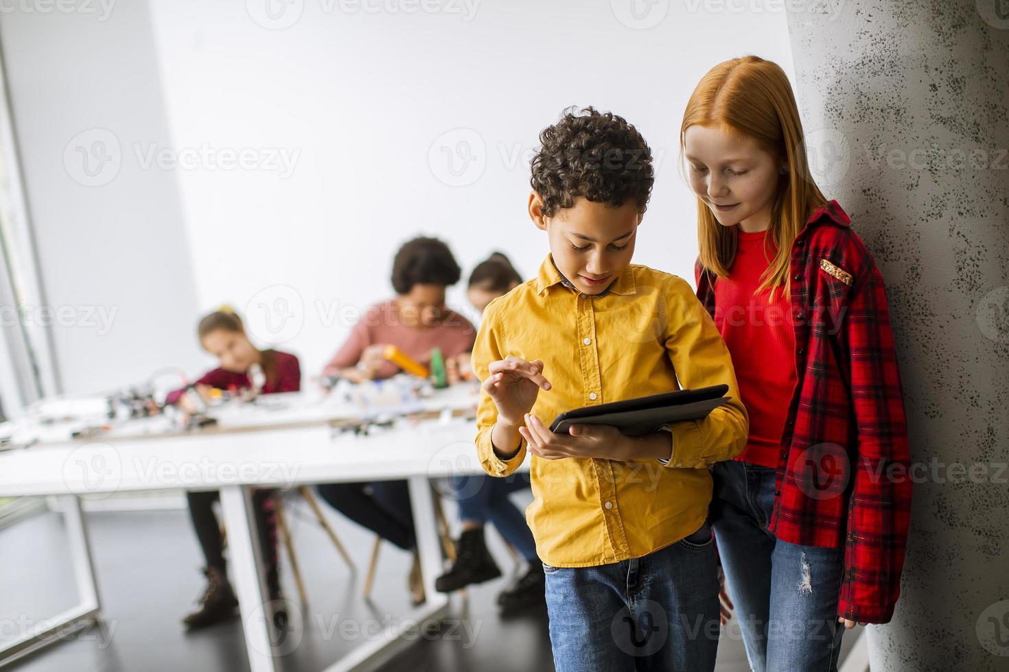 Best friends standing in front of kids programming electric toys and robots at robotics classroom photo