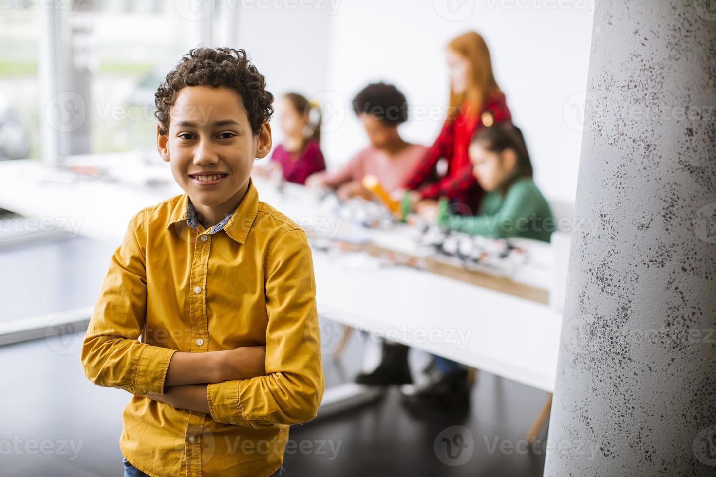 Cute little boy parado frente a los niños que programan juguetes eléctricos y robots en el aula de robótica foto