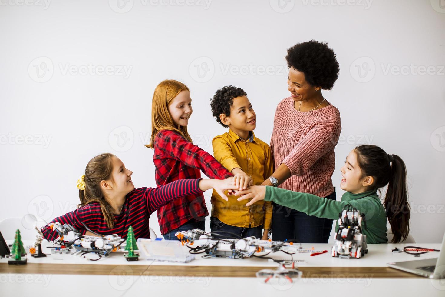 Niños felices con su profesora de ciencias afroamericana que programan juguetes eléctricos y robots en el aula de robótica foto