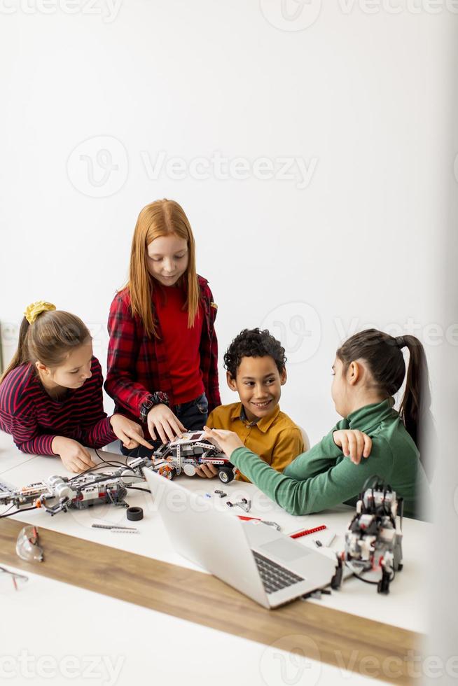 Niños felices programando juguetes eléctricos y robots en el aula de robótica foto