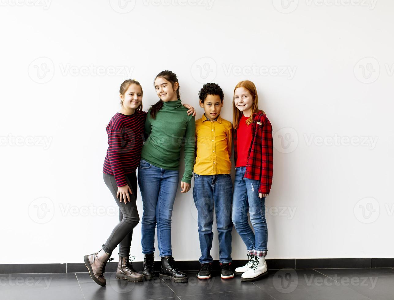 Retrato de niños pequeños lindos en jeans mirando a la cámara y sonriendo de pie contra la pared blanca foto