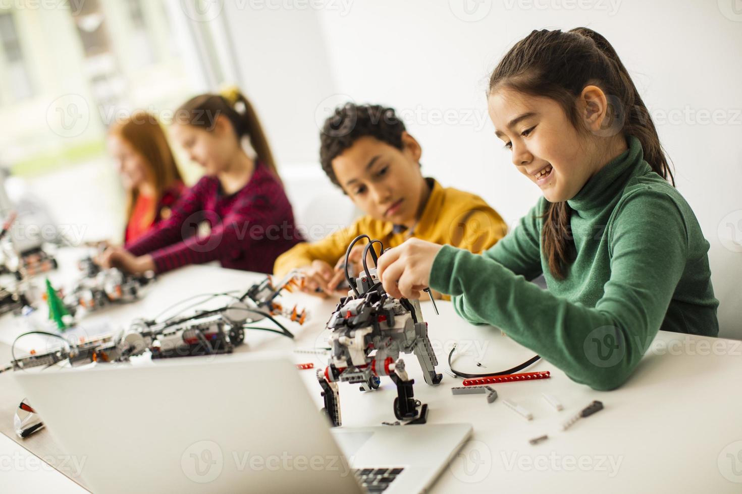 Niños felices programando juguetes eléctricos y robots en el aula de robótica foto