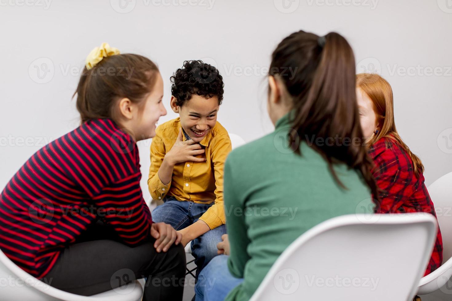 Retrato de lindos niños pequeños en jeans hablando y sentados en sillas contra la pared blanca foto